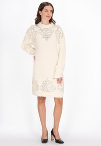 Kötött krémszínű ruha díszes ezüst hímzéssel a vállán és az alján. Hosszú ujjakkal, kerek nyakkivágással és laza szabással rendelkezik.