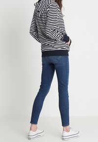 Navyblauwe en witte gestreepte hoodie met een capuchon met trekkoord, geribbelde manchetten, gedragen met donkeblauwe skinny jeans en witte sneakers.