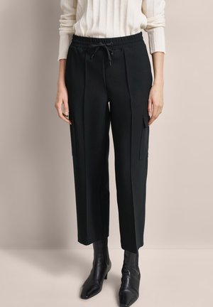 Black, mid-rise trousers with a drawstring waist, side pockets, and a smooth texture, paired with sleek black ankle boots.