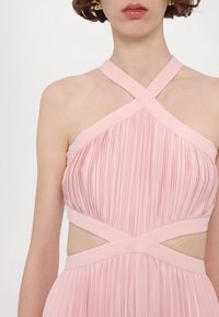 Robe plissée rose avec un décolleté halter croisé, des côtés découpés et une taille lisse, mettant en avant un design fluide.