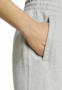 Svetlošedé tepláky s textúrovaným povrchom, s bočnou vreckom a elastickým pásom. Ruka pohodlne spočíva vo vrecku.