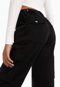 Musta kestävää kangasta valmistetut cargo-housut, joissa on sivutaskut, rento istuvuus ja säädettävä vyötärövö.