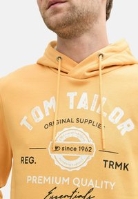 Gelbes Hoodie mit Kordelzug, "Tom Tailor"-Logo und bedruckten Details wie "Premium Quality" und "seit 1962". Aus Baumwollmischung.