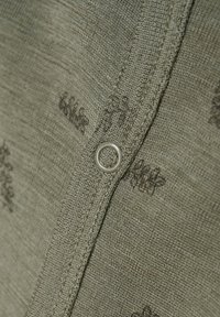 Olivgrön tyg med en texturerad väv, prydd med en silverfärgad metalögla och mörkbruna blommönster längs sömmen.