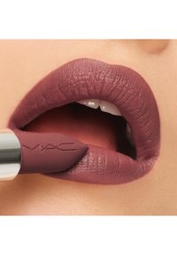 Un rouge à lèvres mauve mat avec une finition texturée est appliqué sur les lèvres. Le tube met en valeur le logo MAC gravé et a une forme lisse et effilée.