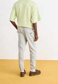  Lichtgroen oversized t-shirt en grijze sweatpants met elastische boorden. De broek heeft een achterzak met een zwart Nike-logo. Bruine schoenen maken de look compleet.