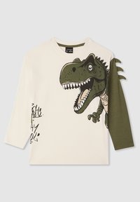 Biała koszulka z graficznym motywem zielonego dinozaura, z długimi oliwkowymi rękawami i kreskówkowymi detalami. Zawiera radosny tekst w stylu graffiti.