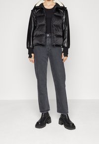 Czarna kurtka puchowa z skórzanymi rękawami i wzorzystym przodem, zestawiona z ciemnoszarymi, prostymi dżinsami oraz masywnymi czarnymi botkami na kostkę.