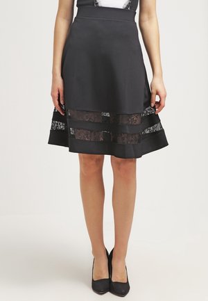 Jupe noire avec une taille ajustée, silhouette évasée, panneaux en dentelle à l'ourlet et accents transparents. Texture lisse, design mi-mollet.