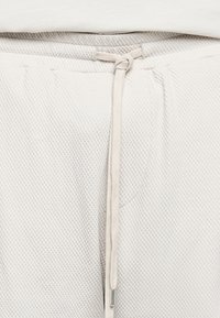 Gros plan sur un pantalon beige en tissu texturé avec un cordon noué à la taille.