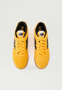 Yellow suede sneakers with black stripes, round toe, textured laces, and rubber soles. Features a white logo tag on the tongue.