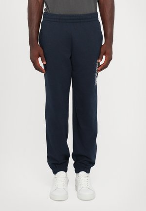 Pantalons de survêtement bleu marine avec une taille élastique et des poignets, dotés d'une poche latérale et d'un accent logo sur la jambe gauche, fabriqués en matériau doux.