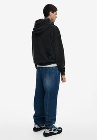 Mørkegrå oversized hoodie med et struktureret design på ryggen, parret med løstsiddende blå jeans og sorte sneakers.