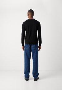 Czarny dzianinowy sweter z długimi rękawami, zestawiony z luźnymi niebieskimi dżinsami, widziany od tyłu na jednolitym tle.