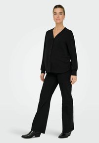 Cardigan noir ample à manches longues avec un col en V et une fermeture à boutons, associé à un pantalon noir évasé assorti et des bottines noires brillantes.