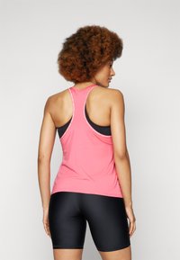 Débardeur de sport rose avec un dos nageur et un soutien-gorge de sport noir en dessous, associé à un short ajusté noir. Texture lisse, détails minimaux.