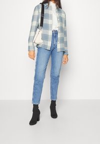 Kraciasta, jasnoniebieska i biała koszula oversize noszona na szarym topie, zestawiona z jasnoniebieskimi spodniami o wysokim stanie i czarnymi botkami na obcasie.