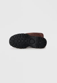 Rjave usnjene čevlje z črnim gumijastim podplatom. Podplat ima teksturiran vzorec za oprijem s izrazitimi drsnikami za oprijem.