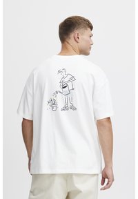 Hvid bomulds T-shirt med en sort stregtegning på ryggen, der skildrer en person, der vander en plante. Kortærmet og afslappet pasform.