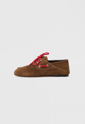 Brown suede moccasin with a low profile, featuring red laces, white eyelets, and contrasting stitching along the seams.