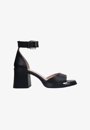 Zwarte leren sandalen met hak, voorzien van een enkelbandje, open teenontwerp, blokhak en metallic accent aan de voorkant. Soepele textuur.