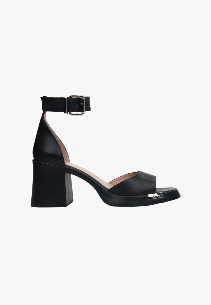 Czarne skórzane sandały na obcasie z paskiem na kostkę, otwarty nos, blokowy obcas i metaliczny akcent z przodu. Gładka faktura.
