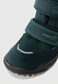 Zielono-czarne dziecięce buty z rzepami, teksturowana tkanina, gumowa podeszwa oraz odblaskowe szare detale w okolicy palców.