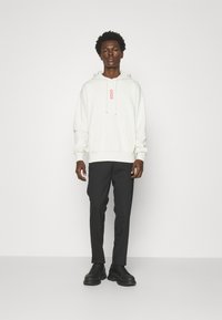 Felpa bianca con logo rosso, abbinata a pantaloni neri e sneakers nere. Caratterizzata da una tasca a marsupio e cappuccio con cordino. Design semplice.