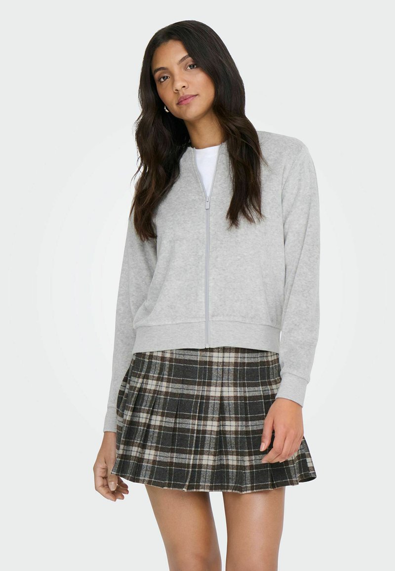 Grauer Sweatshirt mit Reißverschluss und langen Ärmeln, kombiniert mit einem plissierten karierten Minirock in Dunkelgrün, Creme und Braun.