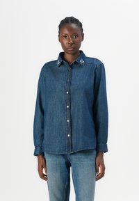 Denim overhemd met een knoopsluiting aan de voorkant, contrasterende parelachtige versieringen op de kraag en lange mouwen. Klassieke blauwe kleur en een relaxte pasvorm.