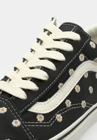 Black canvas sneaker with white lace, featuring a floral pattern of small white daisies with yellow centers and a white leather side stripe.