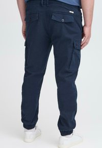 Marineblaue Cargo-Hosen aus Baumwolle mit schmalem Schnitt, ausgestattet mit Seitentaschen, geknöpften Gesäßtaschen und elastischen Bündchen.