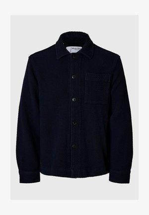 Tumši zila pogu jaka tekstilmateriālā, ar apkakli, priekšējiem kabatām un piecām pogām uz priekšu. Vienkāršs dizains.