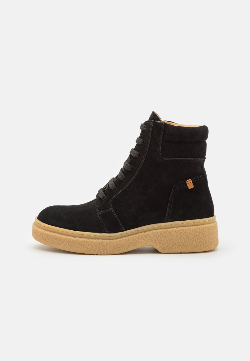 Botas de tobillo negras de ante con una suela de goma texturizada en tono marrón, diseño con cordones y un pequeño logotipo en el costado.