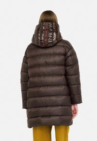 Mørkebrun pufferjakke med shiny finish, vandrette striber og hætte med et logo på bagsiden. Matcher med sennepsfarvede bukser.
