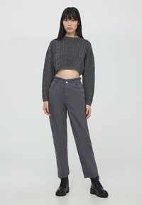 Maglione cropped grigio a maglia con motivo testurizzato, abbinato a pantaloni grigi a vita alta e stivaletti neri con lacci.