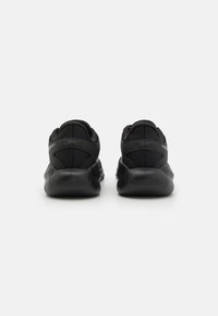 Pantofii sport negri au un superior din plasă și o talpă moale din cauciuc, cu un toc rotunjit și o marcaj minimal pe spate.