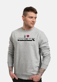 Felpa grigia con maniche lunghe, caratterizzata dalla scritta "I ♥ MINECRAFT" in testo pixelato. Polsini e orlo a coste, tessuto morbido.