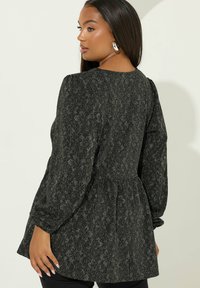 Blusa nera con motivo a stampa e maniche a sbuffo, in tessuto testurizzato. Presenta una vita aderente e una vestibilità ampia. Collo tondeggiante sul retro.