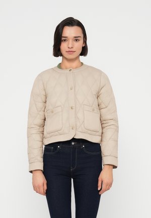 Lys beige quiltet jakke med rund hals, to frontlommer og knappelukking, kombinert med mørke jeans. Jevn tekstur.
