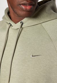 Hoodie Nike vert clair avec une capuche à cordon et un petit logo argenté sur la poitrine. Texture douce avec une coupe décontractée et des manches raglan.