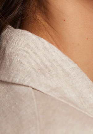 Gros plan sur le col d'un vêtement en lin beige, mettant en valeur le tissu texturé et une finition naturelle et douce contre un ton de peau lisse.