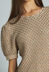 Maglione a maniche corte in beige, con un motivo testurizzato e dettagli lucidi, scollo a onda e polsini a coste aderenti.