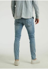 Jasnoniebieskie dżinsy z denimu o dopasowanym kroju, z tylnymi kieszeniami z kanciastymi klapkami, zestawione z casualowym obuwiem.