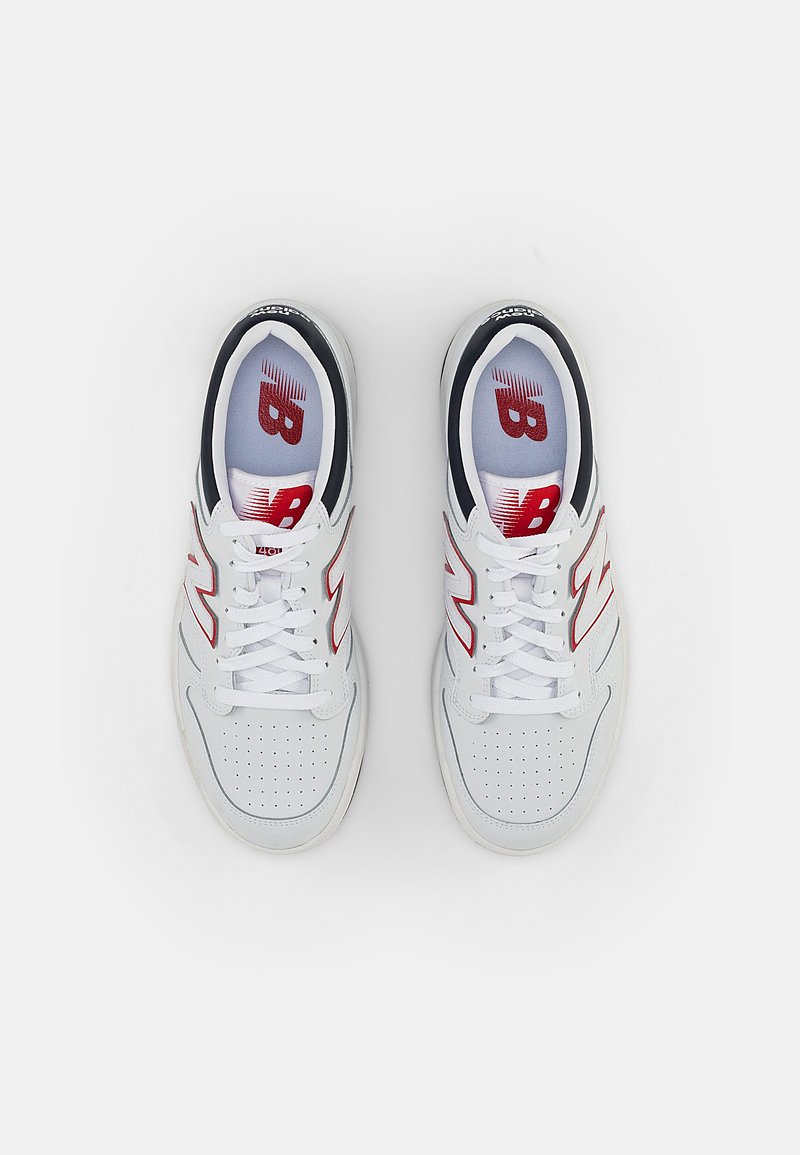 Baskets blanches de sport avec un design perforé, des accents rouges sur les côtés et une doublure intérieure bleu marine avec un logo sur les semelles intérieures.