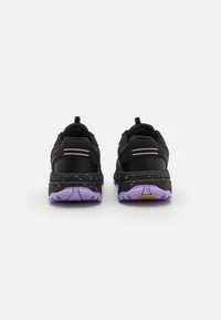 Baskets noires avec des accents violets, présentant une tige texturée, un talon solide et un design de semelle tachetée. Lacets plats et tirant inclus.