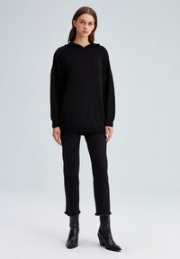 Fekete, oversized kapucnis pulóver, hosszú ujjú, egy darabból készült és texturált felülettel. Fekete, slim-fit nadrággal és magassarkú csizmával párosítva.