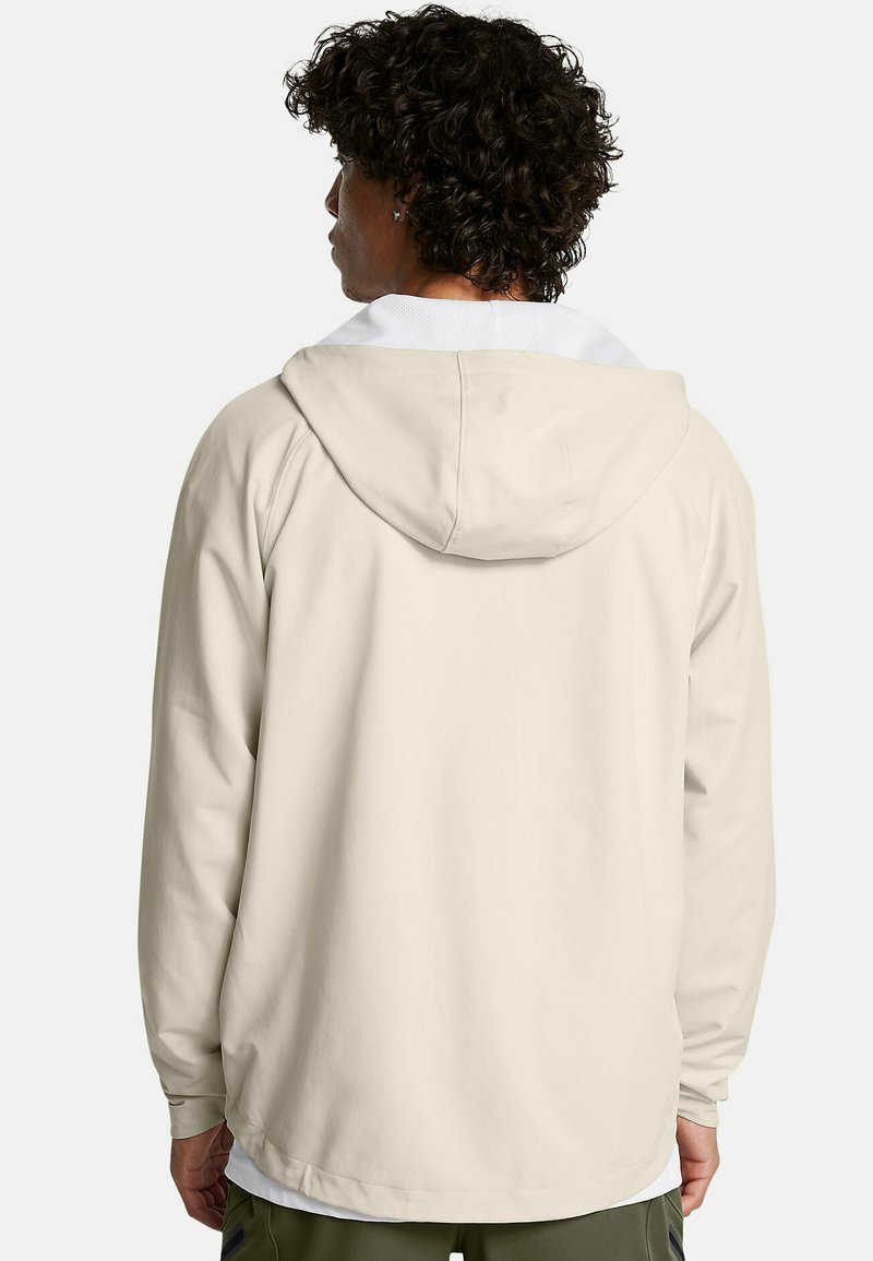 Veste à capuche beige clair avec des manches longues et un design épuré et décontracté. Elle présente une doublure intérieure blanche et une texture douce.