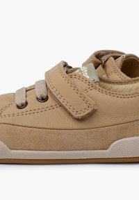 Scarpa in pelle beige con fascia in velcro, dettagli in suede e suola in gomma. Presenta lacci beige e un logo sulla linguetta. Superfici lisce e strutturate.