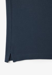 Tejido texturizado azul marino, con aberturas laterales en el dobladillo y un acabado suave. El material parece transpirable y ligero.